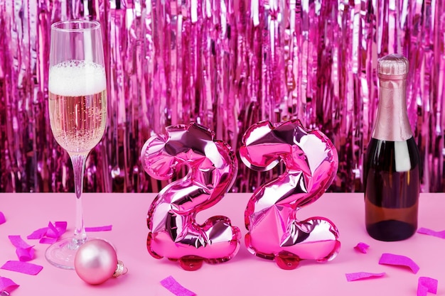 Concept of holidays and the new year. 2022 pink foil balloons, champagne, glass  and confetti