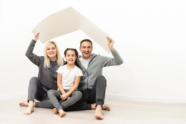 концепция жилья для молодой семьи. Мать, отец и ребенок в новом доме с крышей у пустой кирпичной стены.