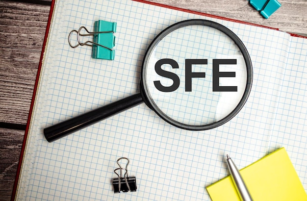 虫眼鏡で白いノートに書かれた会計ビジネスの頭字語 SFE Sales Force Effectiveness のコンセプト イメージ