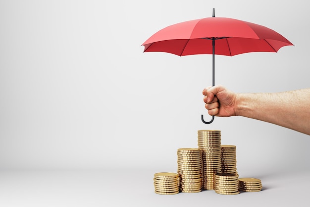 Photo a concept image showcasing a hand holding a red umbrella above stacks of golden coins against a white background symbolizing financial protection