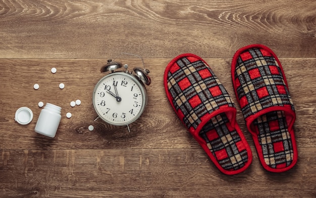 The concept of insomnia. Indoor slippers and alarm clock, pill on the floor. Top view