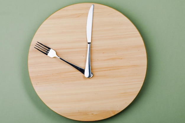 The concept of intermittent fasting and skipping meals Wooden round tray with Cutlery in the form of clock hands The concept of the eighthour window of feeding or the concept of Breakfast time