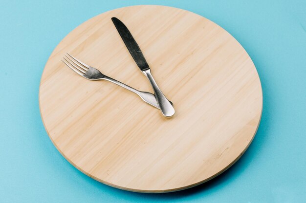 The concept of intermittent fasting and skipping meals Wooden round tray with cutlery in the form of clock hands