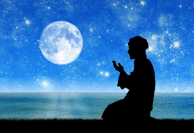 Concept of Islamic culture. Silhouette of man praying on the background of the sea at night