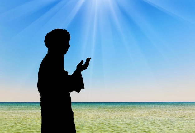 이슬람 문화의 개념입니다. 광선에 바다의 배경에 기도하는 남자의 실루엣