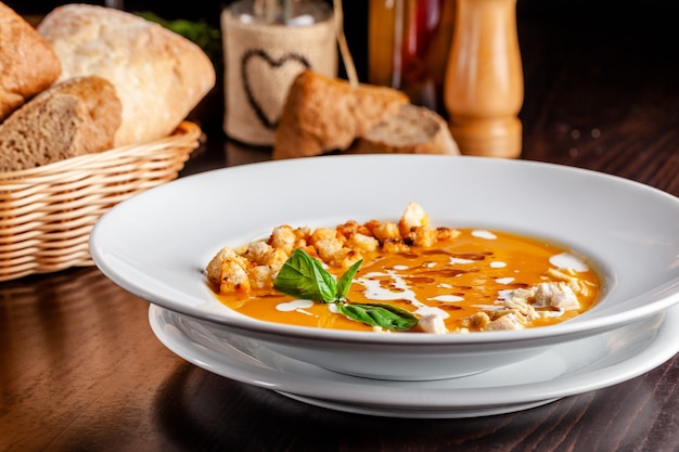 The concept of Italian cuisine. Pumpkin cream soup with orange flavor, chicken pieces, bread croutons and cream. A string of red wine on the table. Serving dishes in the restaurant