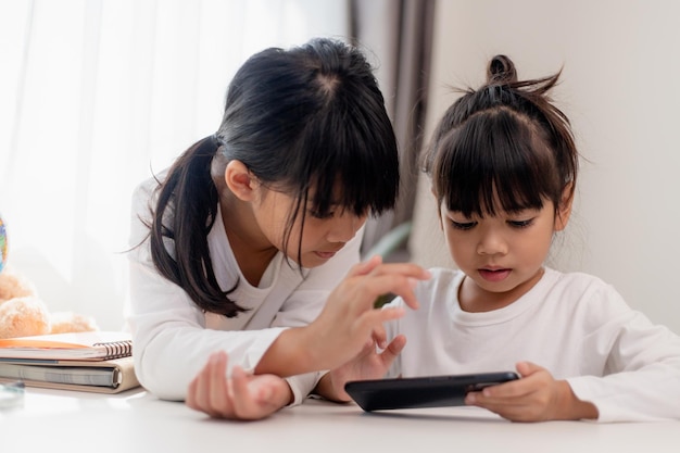 Concept kinderen en gadgets Twee kleine meisjes broers en zussen zussen kijken naar de telefoon en glimlachen Ze houden een smartphone vast video's kijken leren spelletjes spelen online spreken Internet voor kinderen Ouderlijk toezicht