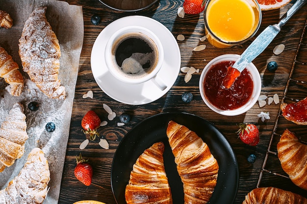 Концепция большого и разнообразного завтрака, различные круассаны и джемы, кофе и амельсиновый сок, грейпфрут и клубника на столешнице