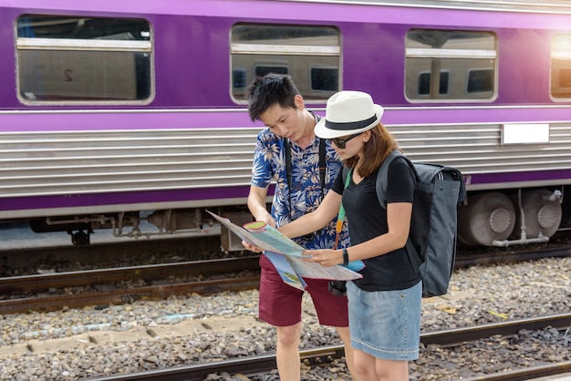 Concept life style travel or journey : young asian couple are\
viewing map to plan a trip in the train station.