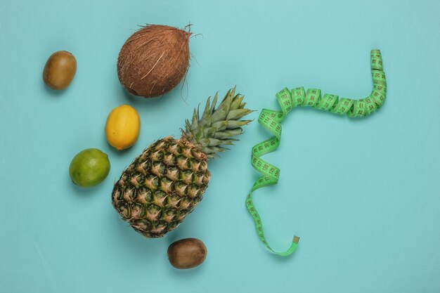 Il concetto di perdere peso. frutti tropicali e nastro di misurazione su sfondo blu. mangiare sano. dieta della frutta. vista dall'alto