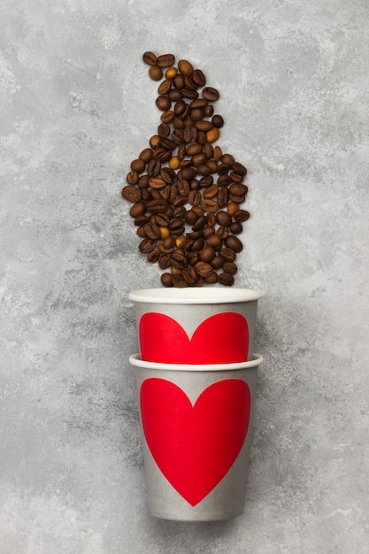 Concept love to coffee. Gray paper cups for drinks with red heart, coffee beans on a light background. Top view. Food background