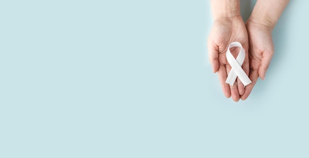 Concept lung cancer awareness Women's hands hold white ribbon on blue background