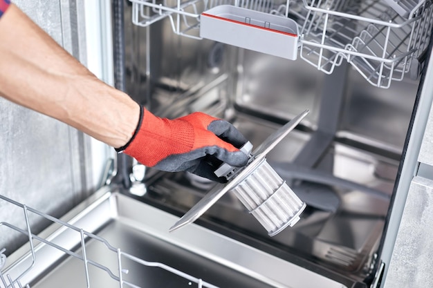 Concept maintenance service of home appliances Worker cleans filter in the dishwasher Male repairman checking food residue filters