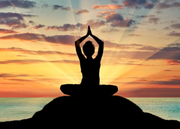 Concept of meditation and relaxation. Silhouette of a girl practicing yoga class on a background of sea sunset