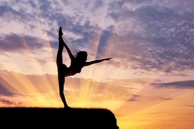 Concept of meditation and relaxation. Silhouette of a girl practicing yoga exercise on the sunset background