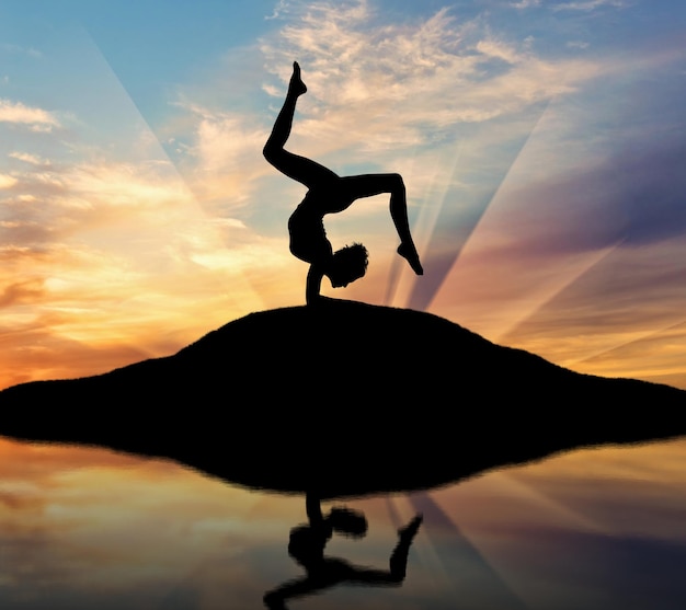 Concept of meditation and relaxation. Silhouette of a girl practicing yoga at sunset and reflection in water