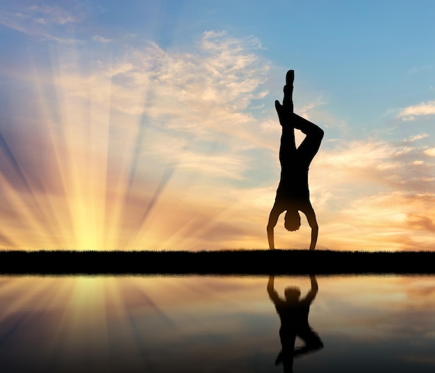 Foto concetto di meditazione e rilassamento. silhouette di un uomo che pratica yoga al tramonto e riflesso nell'acqua