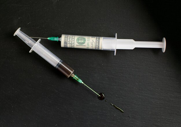 The concept of money and drugs Money in one syringe and a drug in another on a dark background