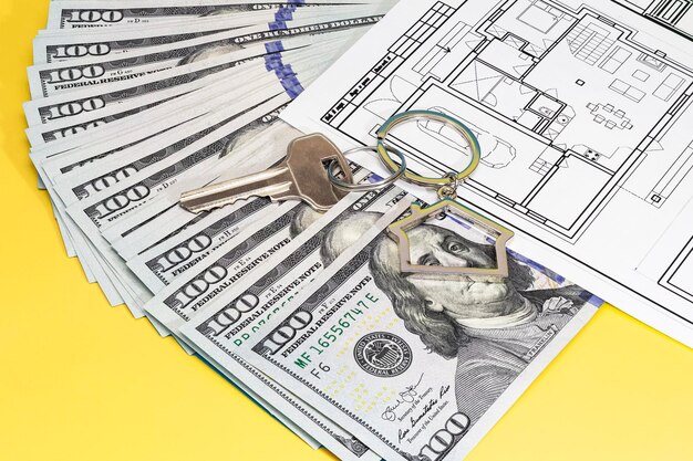 The concept of mortgage and rental housing and real estate Mortgage credit lending Metal keychain with keys and a plan of the house on the laid out dollar banknotes on a blue background