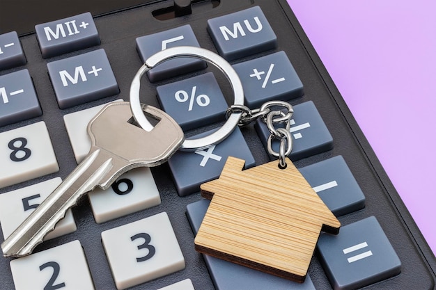 Photo the concept of mortgage sale and rental of housing and real estate mortgage credit lending calculator with keys and a keychain in the form of a house on a gray background banner format copy space