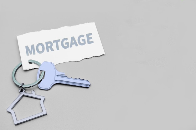 Концепция ипотечной продажи и аренды жилья и недвижимости Ипотечное кредитование Брелок в виде дома с ключом на сером фоне