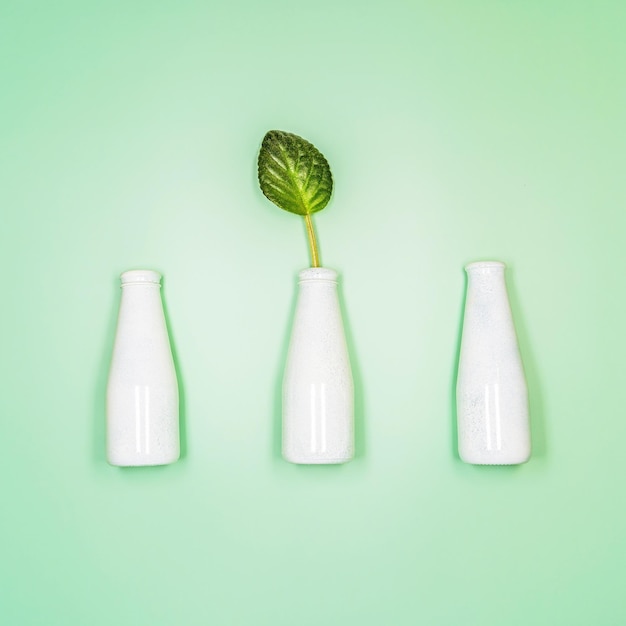 Concept of natural cosmetic with bottles and leaf on light green background