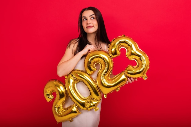 The Concept of the New Year A brunette attractive woman in a dress holds the numbers 2023 from golden balloons