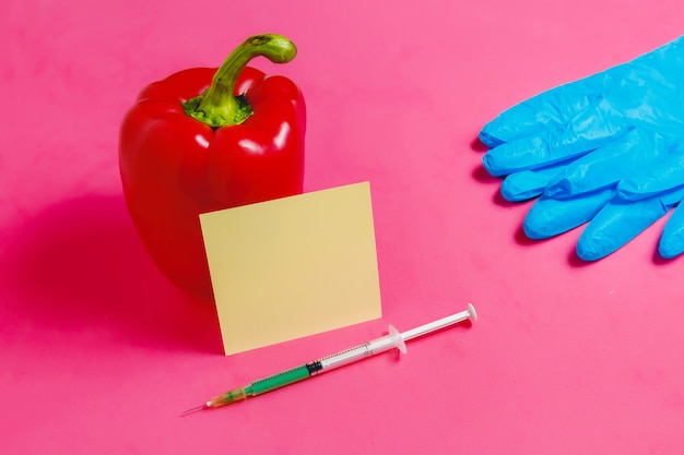 Концепция не натуральных продуктов, ГМО. Шприц, стикер, синие перчатки и красный перец