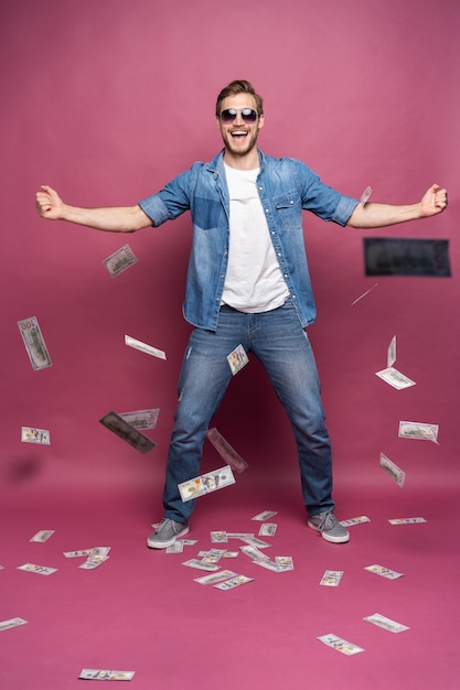 Фото Концепция финансового богатства, процветания и лотерейных выигрышей - человек, выбрасывающий свои деньги, изолированные на розовом фоне