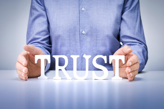 Фото Понятие доверия бизнеса. рука бизнесмена держа деревянные буквы с словом дела доверия на предпосылке таблицы.