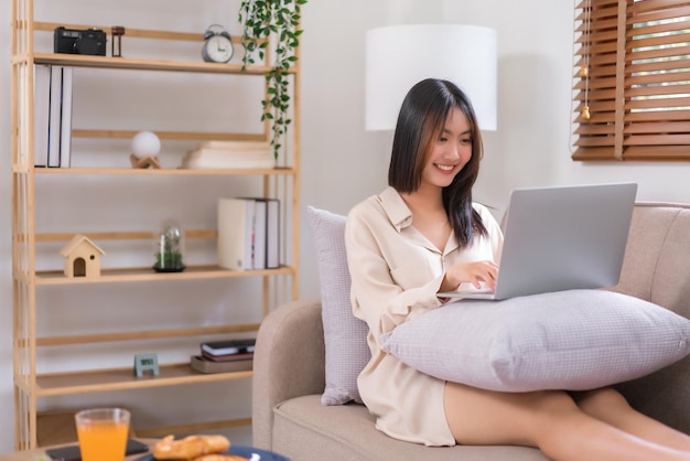 Concept ontspanning thuis Aziatische vrouw die met vrienden op laptop babbelt terwijl het zitten op bank