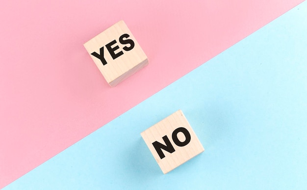 The concept of opposites wooden block with YES NO on blue and pink background flat lay top view