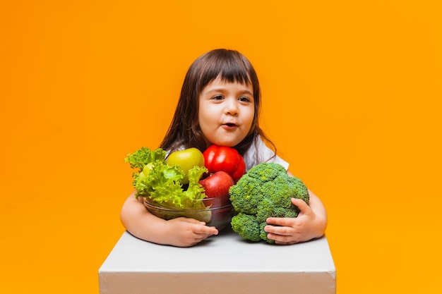 The concept of organic food little girl holding a basket of fruits and vegetables on a yellow background Healthy baby food