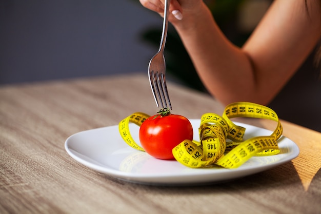 Concept of overweight, tomato and tape measure in a plate