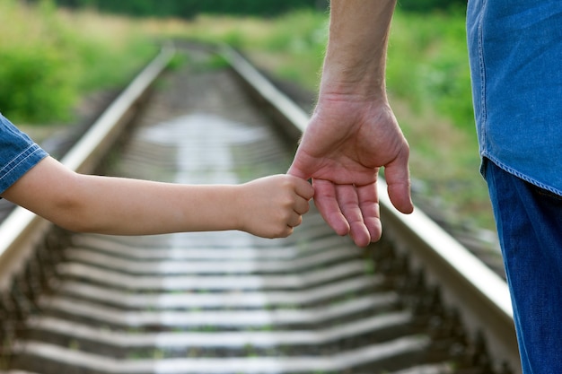 Il genitore concettuale tiene la mano di un bambino piccolo e la ferrovia sul futuro