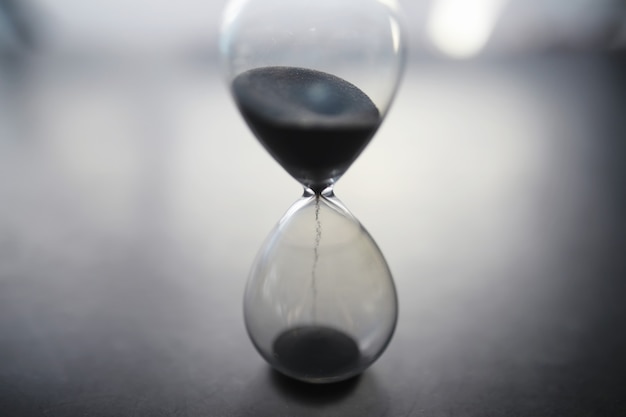 The concept of the passage of time. Hourglass on a dark background. Inscription time. The shadow on the surface of the word.