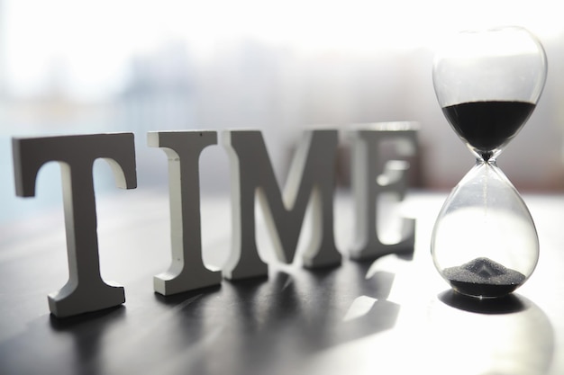 The concept of the passage of time. Hourglass on a dark background. Inscription time. The shadow on the surface of the word.