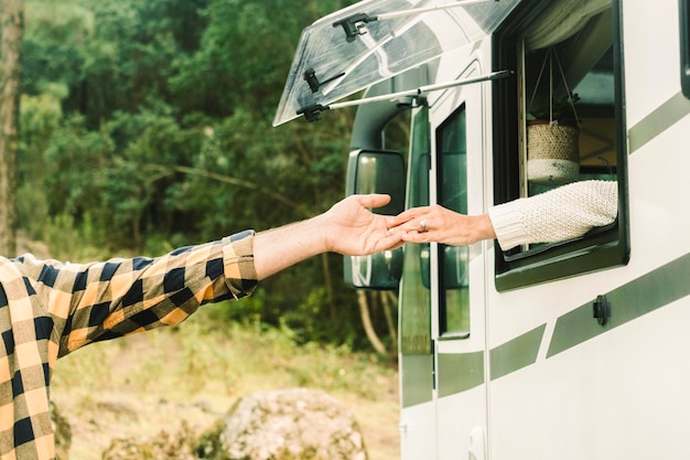 Concept of people travel together with love One man and woman touching hands each other from inside a camper van to outside Green nature forest in background Traveler and destination Vanlife