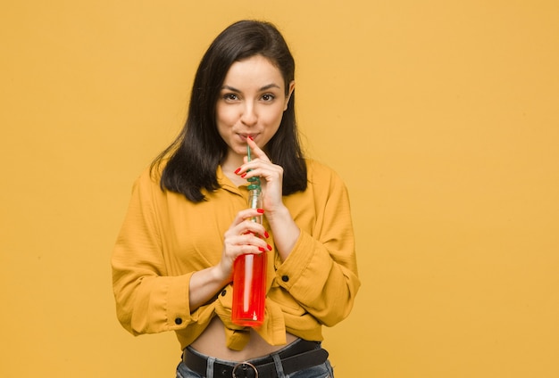 Concept photo of sweet female is drinking cocktails, summertime. Wears yellow shirt, isolated yellow color background.