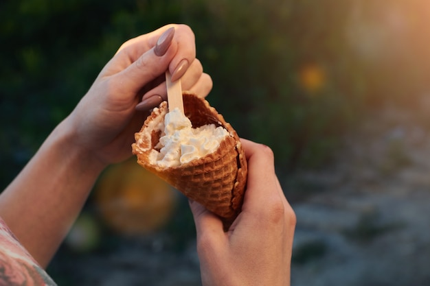 コンセプト写真の女性はアイスクリームを保持します。公園で夏の少女は木のスプーンでアイスクリームを食べます。ライトフレア