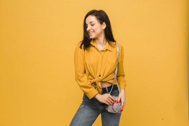 Concept photo of young female with purse, smiling and looks happy. Wears yellow shirt, isolated yellow color background.