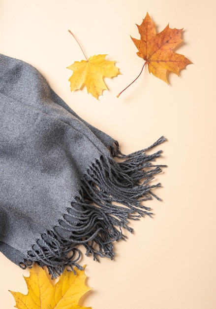 Concept plat lag met herfst esdoorn bladeren en een gezellige grijze sjaal op een lichtoranje achtergrond Bovenaanzicht