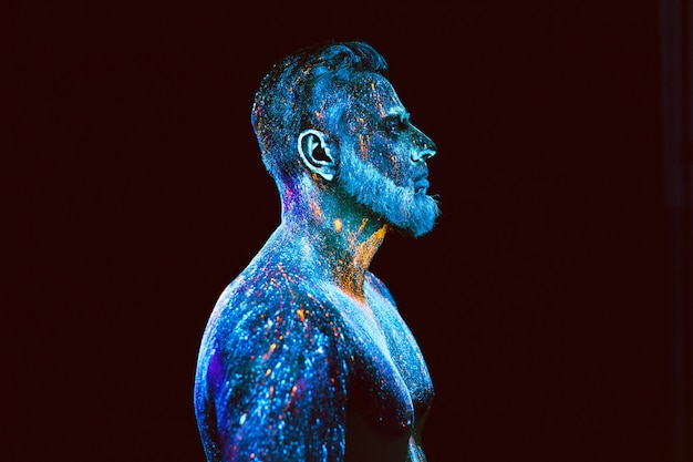 Concept. Portrait of a bearded man. The man is painted in ultraviolet powder.