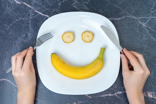 다이어트와 건강한 식생활에 대한 긍정적인 태도의 개념 바나나가 든 접시 위에 칼붙이를 든 여성의 손