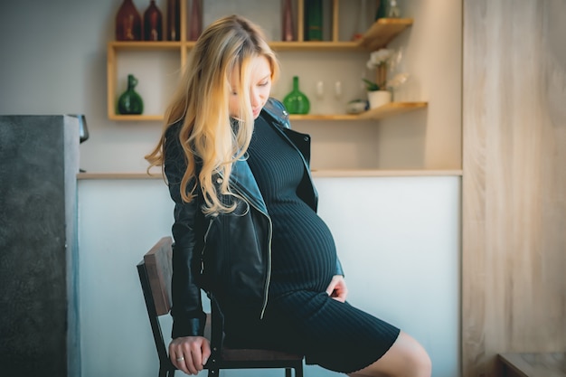 Concept - pregnant belly of caucasian blonde girl in white shirt in white light room