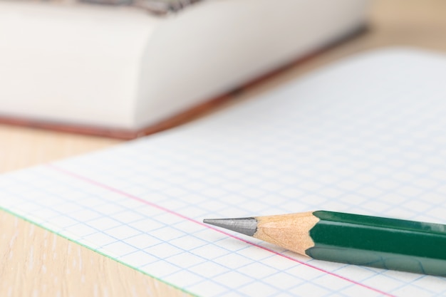 Photo the concept of preparation for school. slate pencil closeup on notebook sheet in a cage.