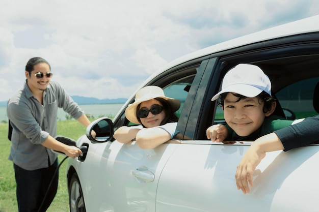 電気自動車とグリーン フィールド湖で進歩的な幸せな家族の概念