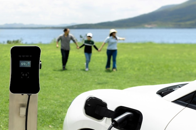 電気自動車とグリーン フィールド湖で進歩的な幸せな家族の概念