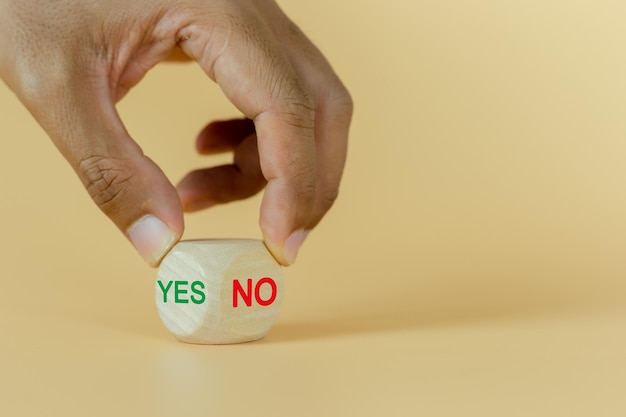 질문 및 답변의 개념 예 또는 아니오라는 텍스트가 있는 나무 큐브 블록을 들고 있는 손은 결정 긍정적인 질문 및 답변의 선택 기호를 선택합니다.