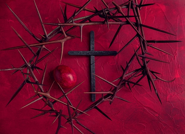 Photo concept red easter background with crown of thorns dyed egg and black wooden cross horizontal image